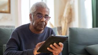 A senior man looking at his mobile tablet device while sitting on sofa.